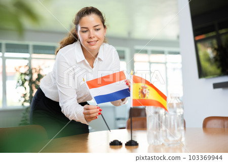 Positive young woman putting little flag of Netherlands on table next to the flag of Spain Positive young woman putting little flag of Netherlands on table next to the flag of Spain 103369944