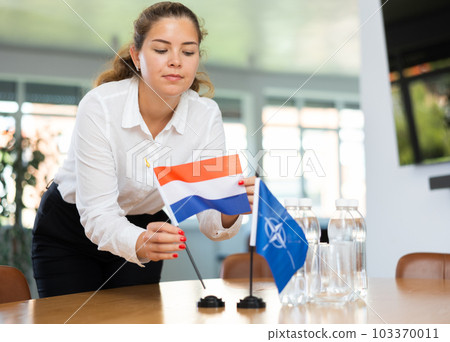 Employee of delegation prepares negotiating table - sets up flag of NATO (OTAN) and Netherlands Employee of delegation prepares negotiating table - sets up flag of NATO (OTAN) and Netherlands 103370011