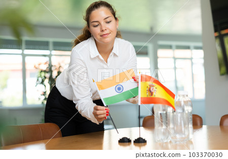 Positive young woman putting little flag of India on table next to the flag of Spain Positive young woman putting little flag of India on table next to the flag of Spain 103370030