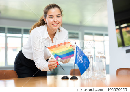 Preparing for business negotiations - woman sets small flags of countries of NATO (OTAN) and LGBT on table 103370055