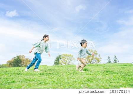 Siblings running on a grassy hill 103370154