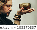 A man with closed eyes listens to the singing bowls. A man holds singing bowls in front of him. The rosary on hand.  Music of Tibetan singing bowls. Himalayan bowls. 103370837