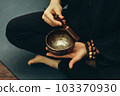 top view of a man sitting in a lotus position with a rosary on his hand playing on singing bowls. Relaxation and meditation. Alternative medicine. Tibetan and Himalayan singing bowls. Making sound. 103370930