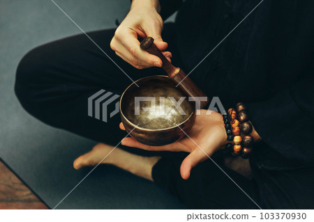 top view of a man sitting in a lotus position with a rosary on his hand playing on singing bowls. Relaxation and meditation. Alternative medicine. Tibetan and Himalayan singing bowls. Making sound. 103370930