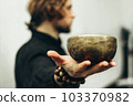 A man holds a singing bowls on his outstretched hand. Music of Tibetan singing bowls. Himalayan bowls. Making sound. 103370982