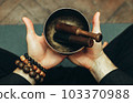 Close-up two hands of a man holding singing bowls with sticks in front of him. Listen to the healing vibrations of Tibetan bowls. Humility and calm. Rosary on the hand 103370988