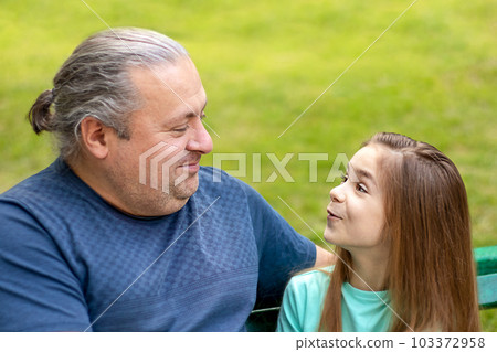 Father and daughter communicate, talk, in the park. Fatherhood, lifestyle, parenting, childhood and family life concept. Father and daughter communicate, talk, in the park. Fatherhood, lifestyle, parenting, childhood and family life concept. 103372958