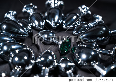 Many metal anal plugs on a black silk sheet.  103373024