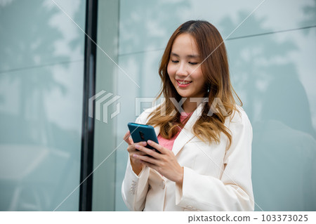 Portrait successful business woman smiling holding smartphone use application chat online in morning, Asian businesswoman working with mobile phone standing against street front building near office 103373025