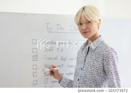Businesswoman marks completed tasks from list on whiteboard 103373872
