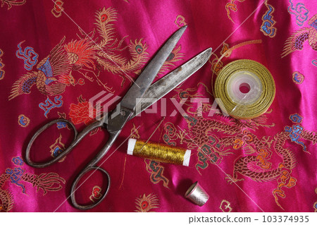 Spool of Gold Thread and Thimble on Vintage Asian Pink Silk Fabric 103374935