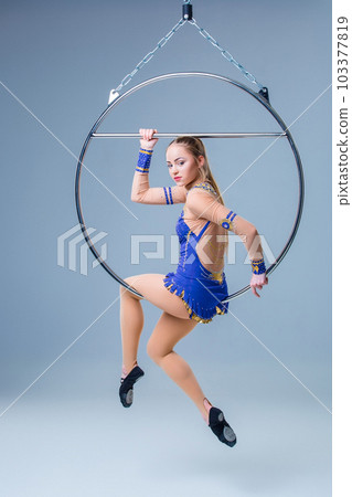 Young woman hanging in aerial ring on a blue background Young woman hanging in aerial ring on a blue background 103377819