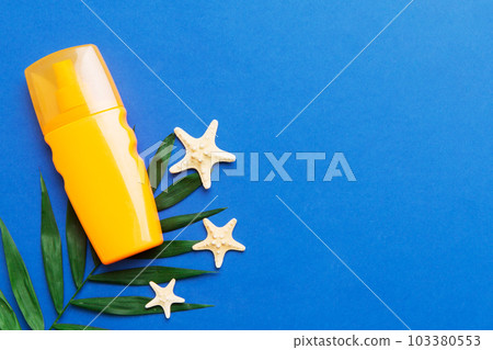 Sunscreen spray bottle. Bottle with sun protection cream and sea shells with tropical green leaf on color background, top view Sunscreen spray bottle. Bottle with sun protection cream and sea shells with tropical green leaf on color background, top view 103380553