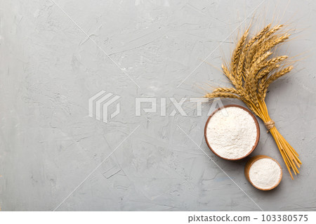 Flat lay of Wheat flour in wooden bowl with wheat spikelets on colored background. world wheat crisis Flat lay of Wheat flour in wooden bowl with wheat spikelets on colored background. world wheat crisis 103380575