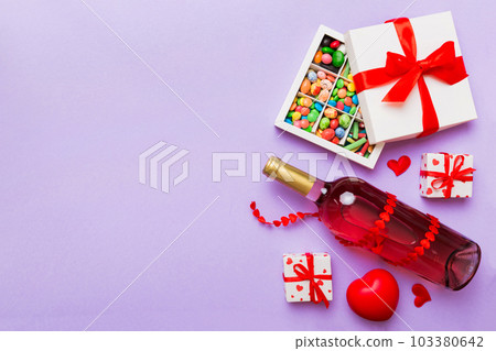 Bottle of red wine on colored background for Valentine Day with gift and chocolate. Heart shaped with gift box of chocolates top view with copy space Bottle of red wine on colored background for Valentine Day with gift and chocolate. Heart shaped with gift box of chocolates top view with copy space 103380642
