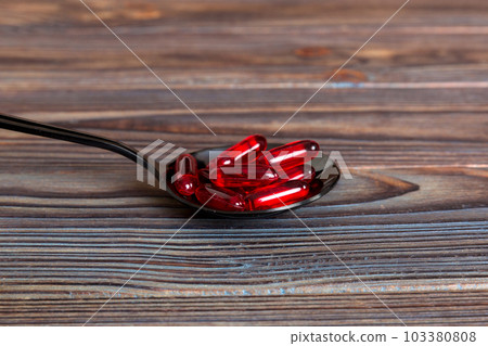 Vitamin capsules in a spoon on a colored background. Pills served as a healthy meal. Red soft gel vitamin supplement capsules on spoon Vitamin capsules in a spoon on a colored background. Pills served as a healthy meal. Red soft gel vitamin supplement capsules on spoon 103380808