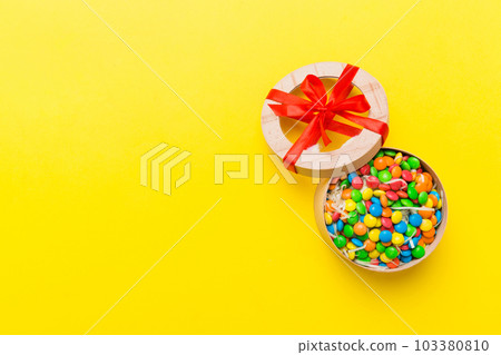 Set of different sweet candy in a paper box with a satin ribbon on a colored background. Holiday concept Set of different sweet candy in a paper box with a satin ribbon on a colored background. Holiday concept 103380810