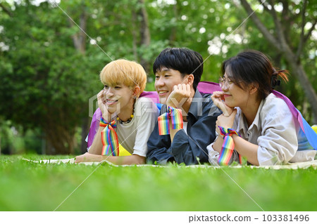 Group of LGBTQ people with pride rainbow flag, lying on green grass. LGBTQ community, freedom, solidarity and equal rights 103381496