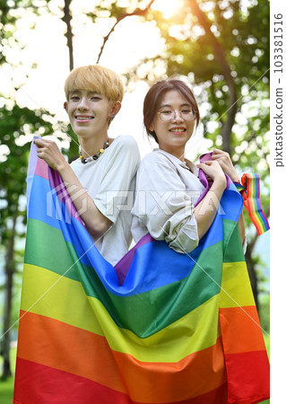 Image of young people with LGBTQ pride flag standing outdoor, supporting LGBTQ community and equality social 103381516