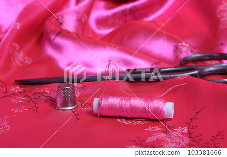Spool of Pink Thread and Thimble on Vintage Pink Satin Fabric Spool of Pink Thread and Thimble on Vintage Pink Satin Fabric 103381666