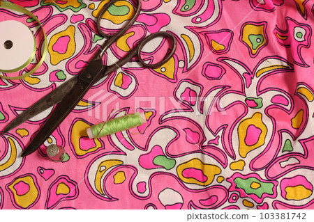 Spool of Green Thread, Thimble and Needle on Retro Pink and Green Fabric Spool of Green Thread, Thimble and Needle on Retro Pink and Green Fabric 103381742