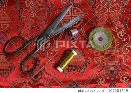 Spool of Gold Metallic Thread and Thimble on Vintage Red Silk Fabric Spool of Gold Metallic Thread and Thimble on Vintage Red Silk Fabric 103381749