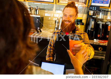 Professional barista young redhaired ginger bearded man in black apron working in coffee shop 103382307