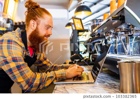 Professional barista young redhaired ginger bearded man in black apron working in coffee shop 103382365