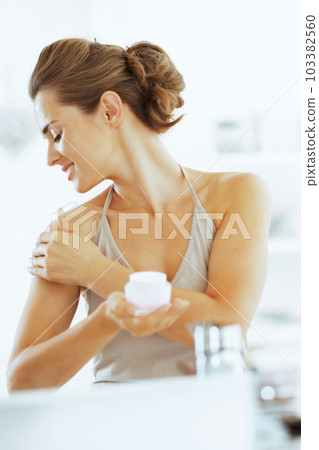 Happy young woman applying cream in bathroom Happy young woman applying cream in bathroom 103382560