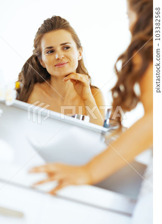 happy young woman checking facial skin condition 103382568