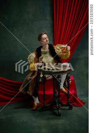 Young man in vintage clothing, royal person, princess sitting and drinking beer with wish against dark green, vintage background Young man in vintage clothing, royal person, princess sitting and drinking beer with wish against dark green, vintage background 103383080
