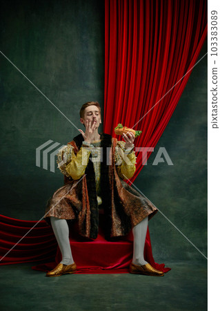Yummy. Young man in vintage clothing eating hot dog against dark green, vintage background. Diet Yummy. Young man in vintage clothing eating hot dog against dark green, vintage background. Diet 103383089