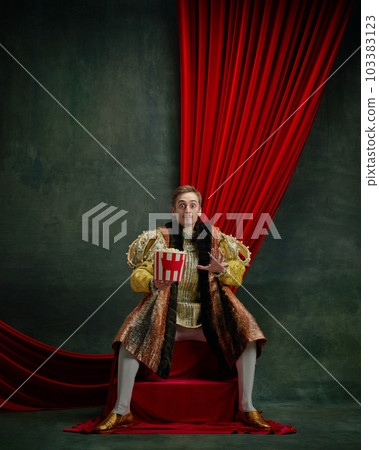 Horror. Portrait of young man emotionally watching movie with popcorn against dark green, vintage background 103383123