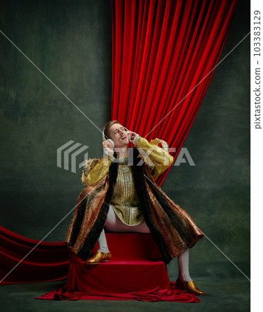 Portrait of young man, royal person, prince listening to music in headphones and singing against dark green, vintage background 103383129