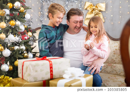 Dad with his son and daughter are sitting on the couch 103385805