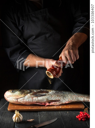 The chef prepares carp herring in the restaurant kitchen. The cook sprinkles pepper on the fish. Work environment on the kitchen table. The chef prepares carp herring in the restaurant kitchen. The cook sprinkles pepper on the fish. Work environment on the kitchen table. 103386407