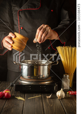 Cooking delicious soup for lunch. Working environment in the kitchen. The chef adds salt to the stock pot. Cucina italiana. 103386473