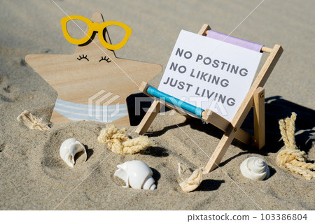NO POSTING NO LIKING JUST LIVING text on paper greeting card on background of beach chair lounge starfish summer vacation decor. Concept of social media technology detox Sandy beach sun. Holiday NO POSTING NO LIKING JUST LIVING text on paper greeting card on background of beach chair lounge starfish summer vacation decor. Concept of social media technology detox Sandy beach sun. Holiday 103386804