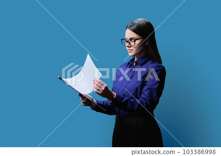 Young business woman holding clipboard, on blue background Young business woman holding clipboard, on blue background 103386998