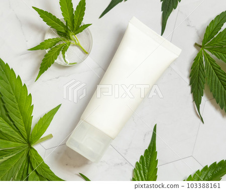 Blank Cream tube near green cannabis leaves on white table, top view. Cosmetic Mockup 103388161