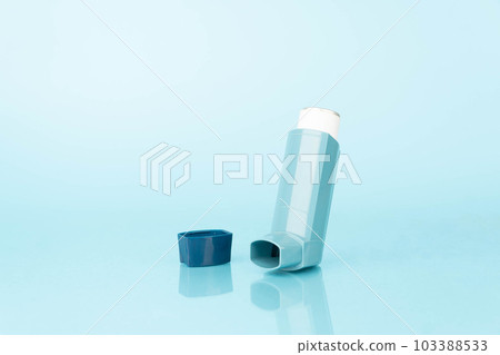 Asthma inhaler with reflection on blue background. Pharmaceutical product contains bronchodilator for treat or prevent asthma attack. World Asthma Day. Asthma inhaler with reflection on blue background. Pharmaceutical product contains bronchodilator for treat or prevent asthma attack. World Asthma Day. 103388533