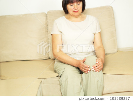 Unhappy senior woman suffering from knee pain on a sofa. People, health care and problem concept. 103389227