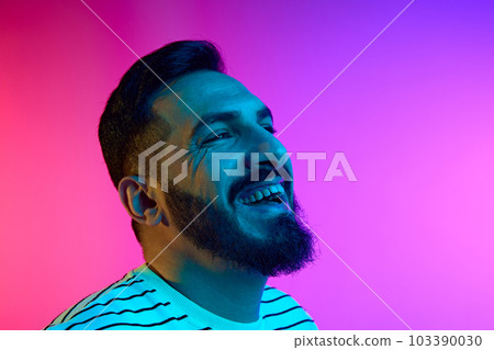 Portrait of bearded handsome man cheerfully smiling against gradient studio background in neon light. Happiness, positive vibe 103390030