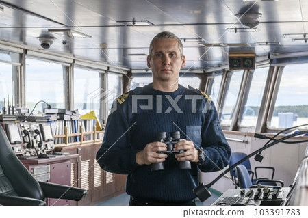 Deck officer with binoculars on navigational bridge. Seaman on board of vessel. Commercial shipping. Cargo ship. Deck officer with binoculars on navigational bridge. Seaman on board of vessel. Commercial shipping. Cargo ship. 103391783