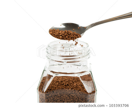 Granulated instant coffee is poured from a spoon into a glass jar of coffee. 103393706