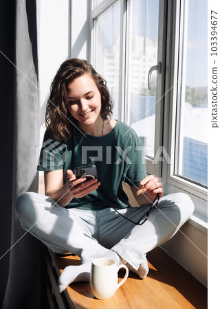 Lockdown Lifestyle: Young Woman Using Smartphone at Home, Engaging in Relaxation and Connection 103394677