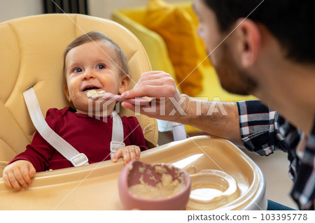 Baby eating her dinner with dad, unrecognizable father feeding toddler kid. 103395778