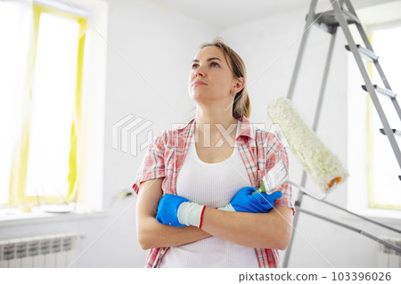 Positive woman holding dirty roller and brush after painting walls in room 103396026