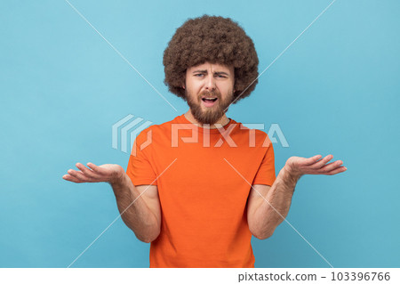 Portrait of stressed annoyed man with Afro hairstyle wearing orange T-shirt standing raised arms and asking, expressing negative emotions. Indoor studio shot isolated on blue background. Portrait of stressed annoyed man with Afro hairstyle wearing orange T-shirt standing raised arms and asking, expressing negative emotions. Indoor studio shot isolated on blue background. 103396766