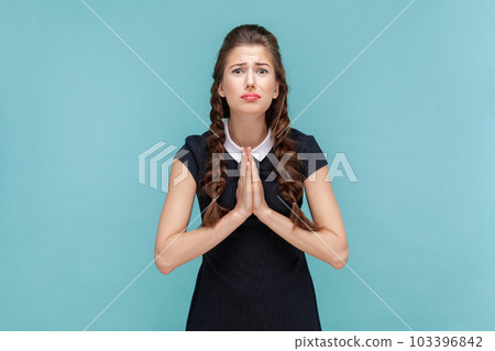 Portrait of hopeful uneasy woman with braids begging for forgiveness keeps palms in praying gesture, asks mercy and says please, needs your help. woman Indoor studio shot isolated on blue background Portrait of hopeful uneasy woman with braids begging for forgiveness keeps palms in praying gesture, asks mercy and says please, needs your help. woman Indoor studio shot isolated on blue background 103396842